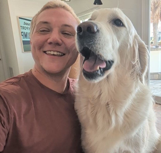 George smiling next to a golden retriever indoors