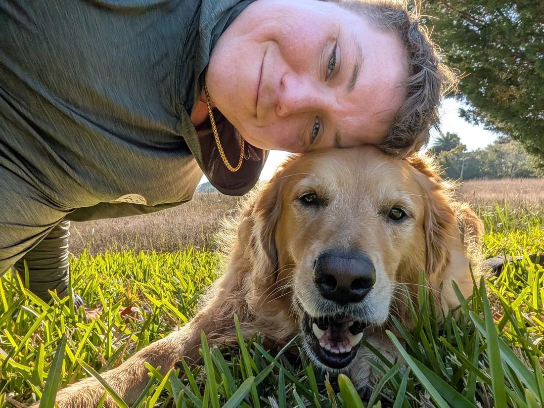 George lying in the grass cheek to cheek with a golden retriever